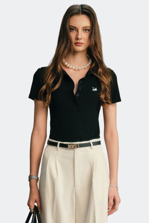 Woman wearing a black polo shirt with a logo and beige pants against a beige background